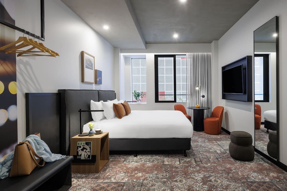 A modern hotel room with a large bed, a desk, a chair, a TV, and a window with curtains.