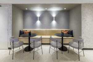 Una sala de reuniones moderna con un sofá central, cuatro sillas grises y dos mesas redondas.
