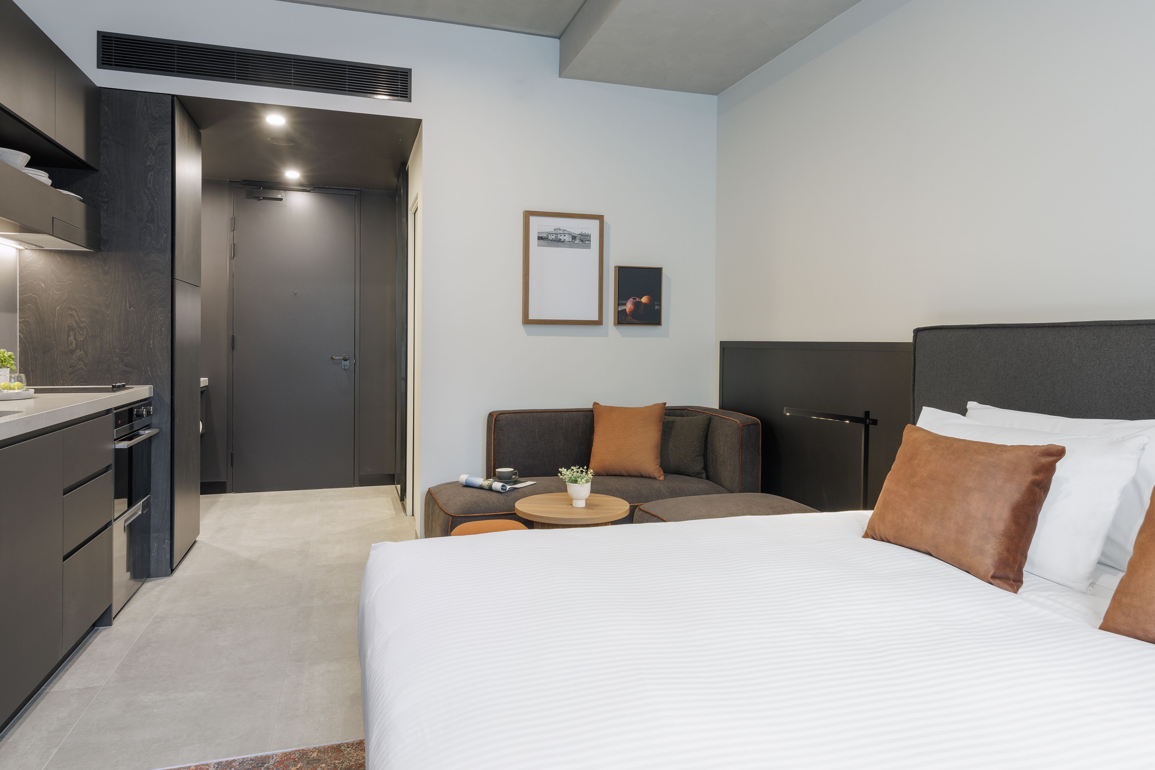 Ein modernes Hotelzimmer mit einem großen Bett, einer Couch, einem kleinen Tisch mit Pflanze und einer Küchenzeile.