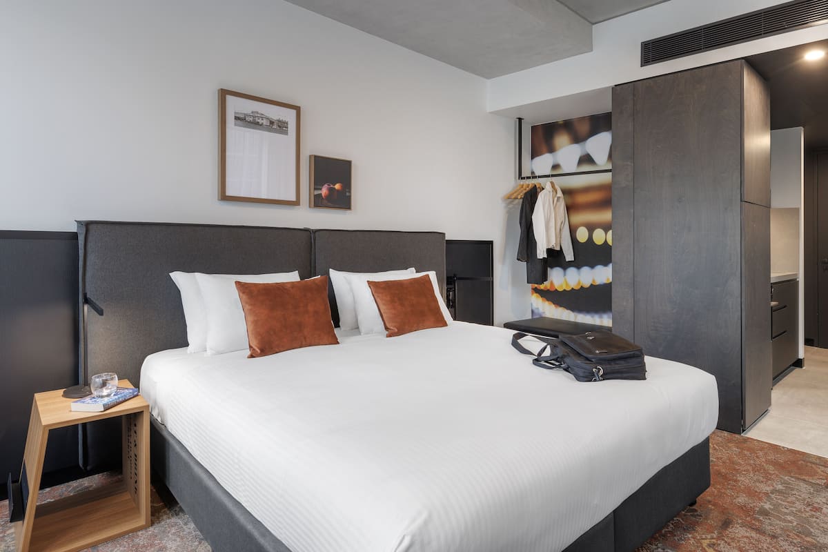 A modern hotel room with a large bed, a bedside table, and a wardrobe.