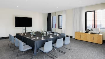 Ein Konferenzraum mit einem langen Tisch, Stühlen, einem Fernseher, Fenstern und einem Schrank.