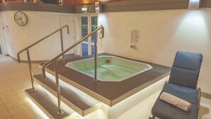 Een wellnessruimte met een jacuzzi, een stoel met een handdoek en een trap met leuningen.