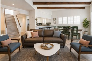 Ett modernt vardagsrum med en brun lädersoffa, två fåtöljer, ett soffbord och en trappa som leder upp till en övre våning.