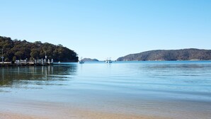 A calm waterfront with boats, a dock, and a forested hill in the background. - Beach Front House Outdoor Hot Tub Sauna Stunning Views (Patonga)