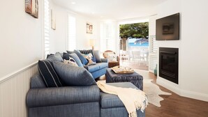 A modern living room with a sectional sofa, ottoman, fireplace, and a view of the outdoors. - Beach Front House Outdoor Hot Tub Sauna Stunning Views (Patonga)