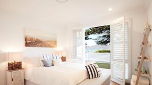 A bedroom with a large bed, a nightstand, a ladder, and a view of the outdoors. - Beach Front House Outdoor Hot Tub Sauna Stunning Views (Patonga)