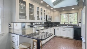 A modern kitchen with white cabinetry, a large island with stools, and a view of greenery outside. - Westport Gem - walk to shops, dining, town center, pet-friendly (Westport)