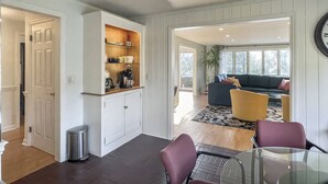 A modern kitchen with white cabinetry, a built-in coffee station, and a dining area with a glass table and purple chairs. - Westport Gem - walk to shops, dining, town center, pet-friendly (Westport)