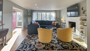 A living room with a sofa, two yellow armchairs, a coffee table, a TV mounted above a fireplace, and a patterned rug. - Westport Gem - walk to shops, dining, town center, pet-friendly (Westport)