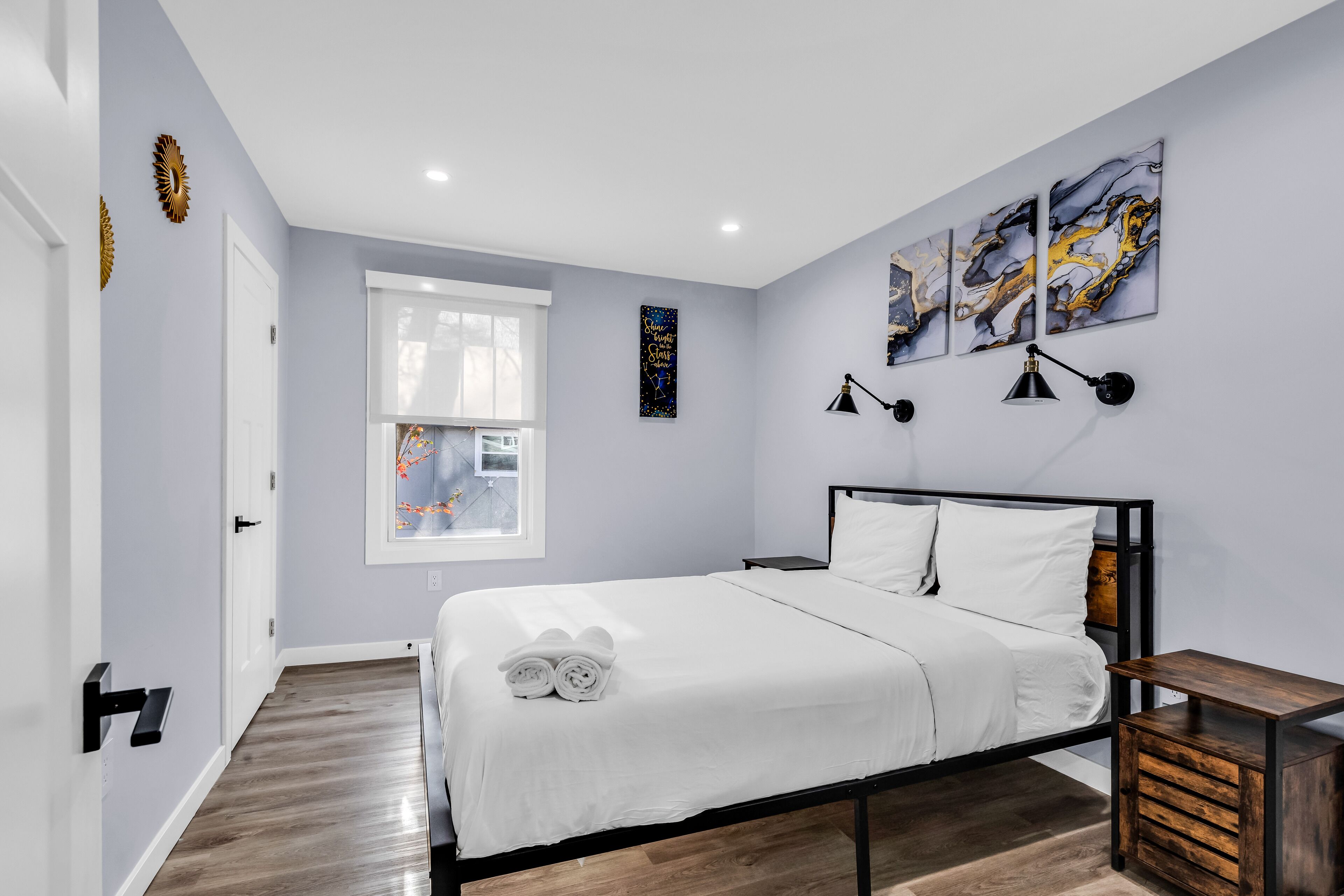 Quarto moderno com cama, mesas de cabeceira e obras de arte nas paredes.