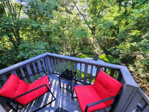 A deck with red cushioned chairs and a small table, surrounded by lush greenery. - Luxury 3BR House in Charlotte (Charlotte)