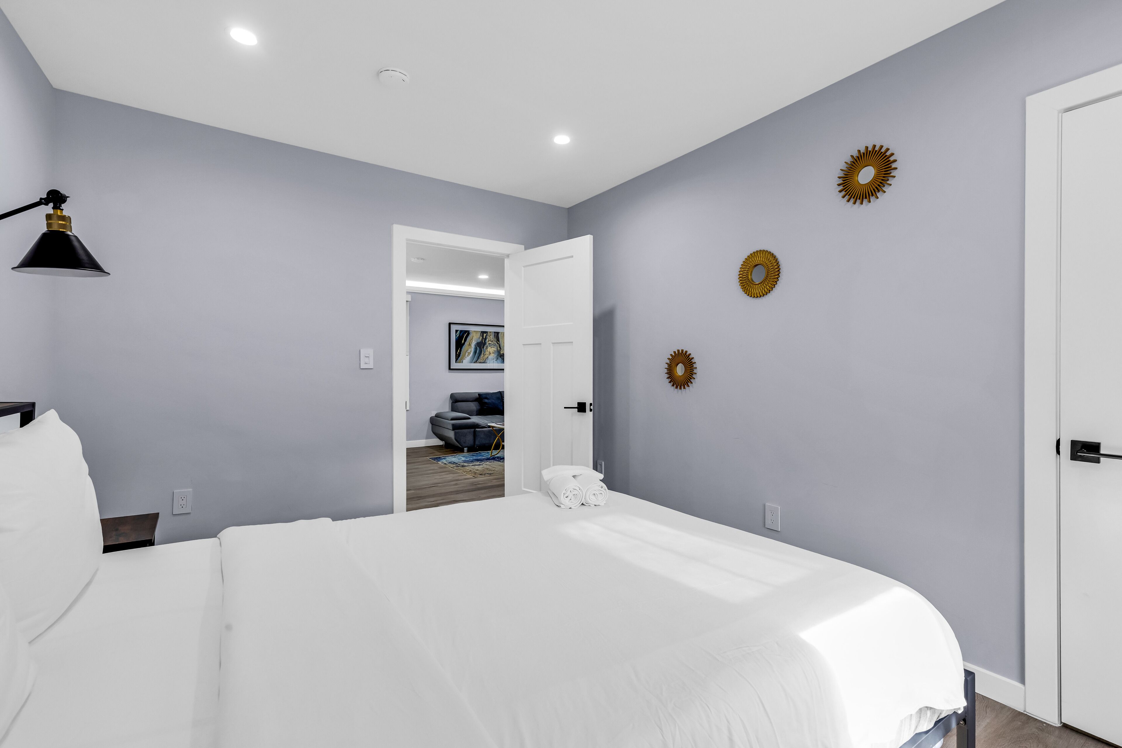 A bedroom with a large bed, a desk, and a chair. There is a door leading to another room.