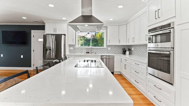 A modern kitchen with white cabinetry, stainless steel appliances, a large island, and a view of greenery outside.