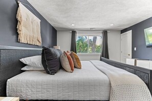 A modern bedroom with a large bed, a headboard, a bedside table, and a window with curtains.