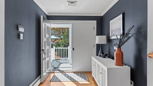A hallway with a wooden floor, a white door leading to a balcony, and a white console with a vase and a lamp.