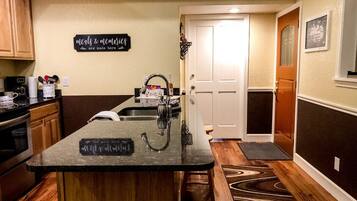 A kitchen with a central island, wooden cabinets, a coffee maker, and a sign that reads "meals & memories are made here."