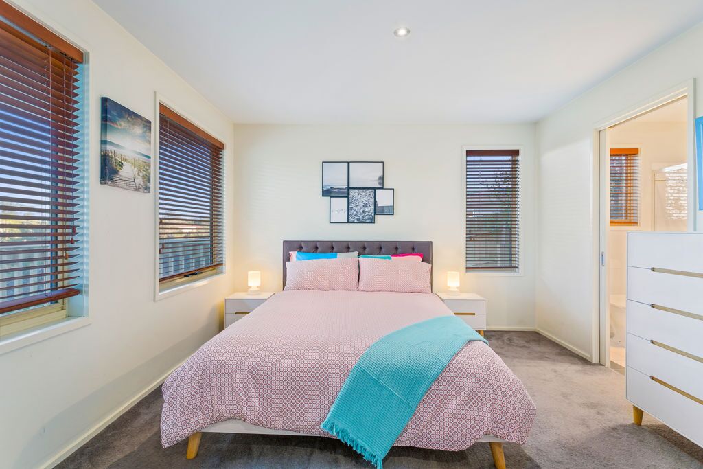 Une chambre à coucher comprenant un lit, des tables de chevet, une commode et une fenêtre avec des stores.