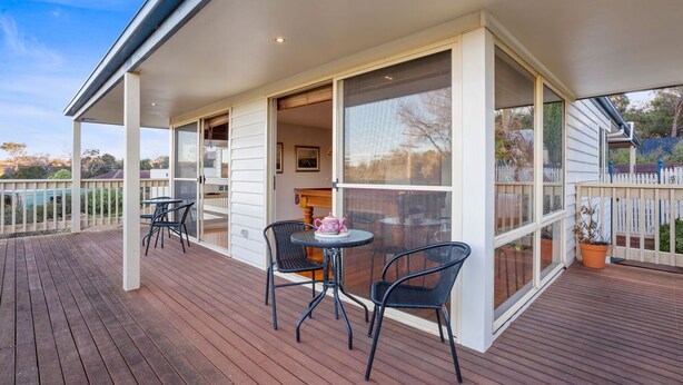 Un espace extérieur abrité, doté d’une terrasse en bois, de deux tables avec des chaises et d’une plante en pot.