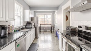 Una cocina moderna con armarios blancos, horno empotrado, cafetera y una ventana con persianas.