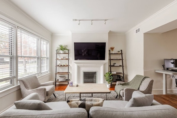A modern living room with a fireplace, a TV mounted above it, and a desk with a computer.