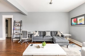 A modern living room with a grey sectional sofa, a white coffee table, and a desk with a chair.