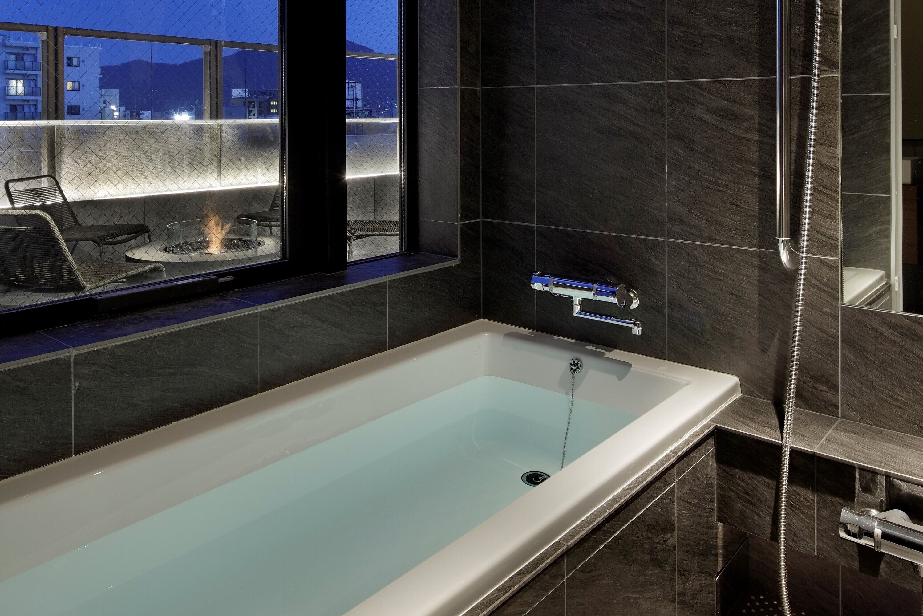 A modern bathroom with a bathtub, a shower, and a seating area with a fire feature.