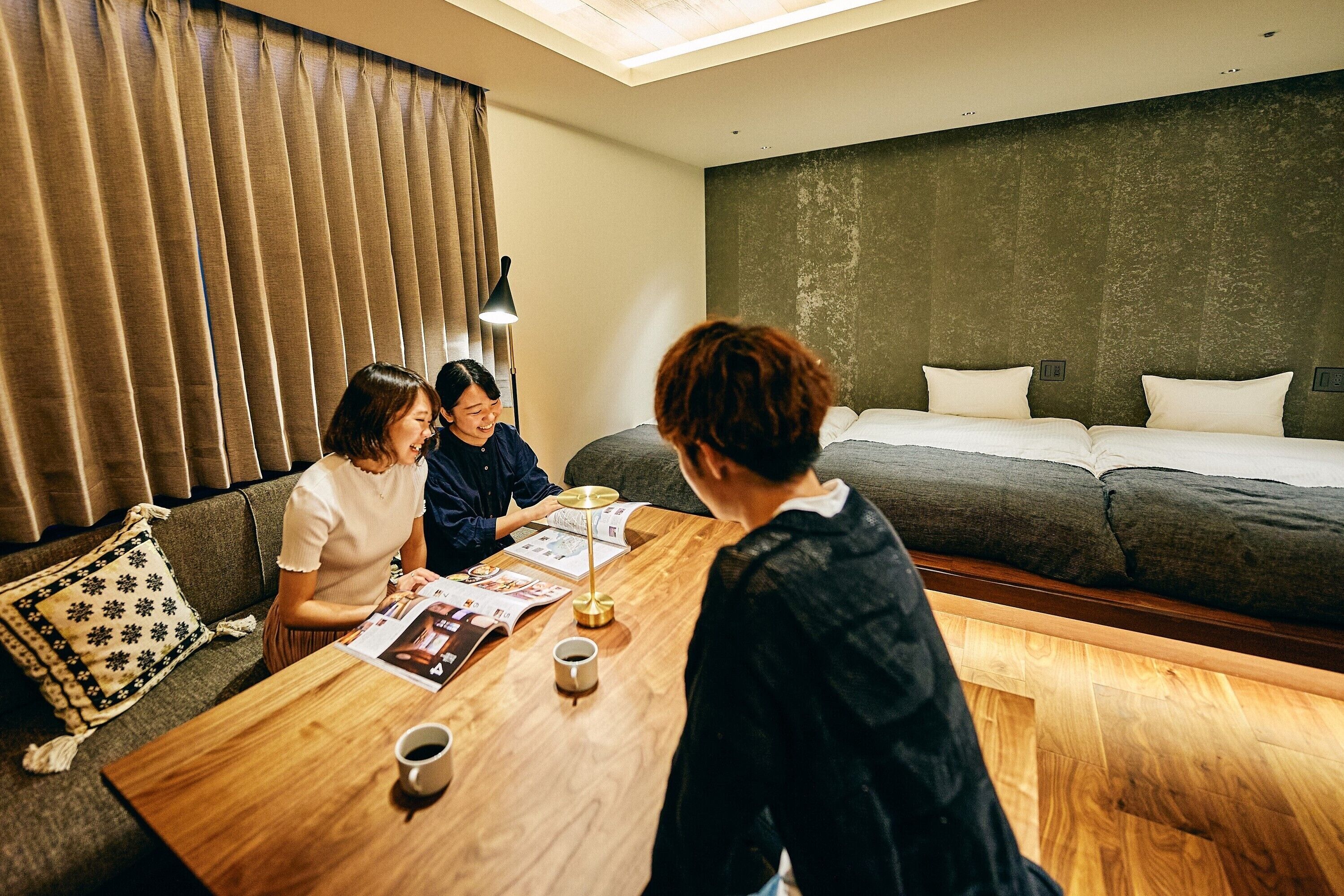 Quarto de hotel com uma mesa de centro de madeira, um sofá com almofadas estampadas e uma cama com lençóis brancos.