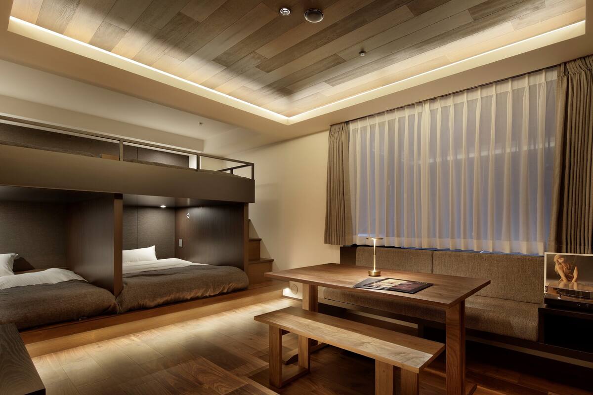 A modern bedroom with a bunk bed, a wooden desk, a bench, and a fireplace.