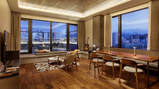 A spacious living area with a wooden floor, a long dining table, and multiple seating options. Large windows offer a view of the cityscape and mountains. - 41PIECES Sapporo (Sapporo)