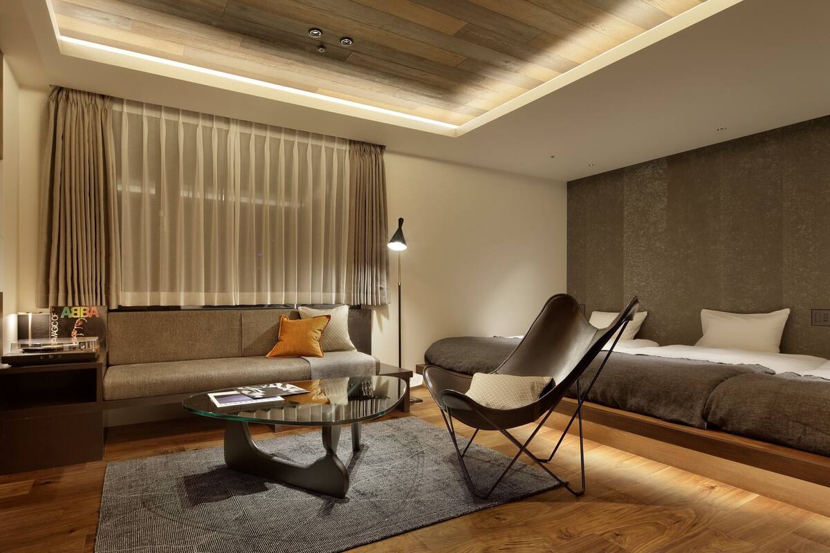 A modern hotel room with a sofa, a bed, a glass coffee table, and a chair.