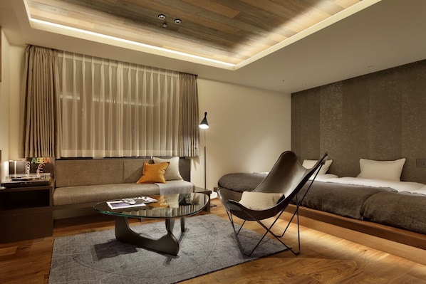 Una habitación de hotel moderna con sofá, cama, mesa de centro de vidrio y una silla.