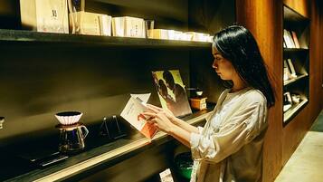 Eine Person liest ein Buch in einem Raum mit Bücherregalen, einer Kaffeemaschine und einem gerahmten Bild.