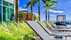 Un espace de détente aménagé sur le toit, avec des chaises longues, une piscine et des palmiers.