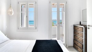 Ein Schlafzimmer mit Bett, Schminktisch und Meerblick durch eine Tür.