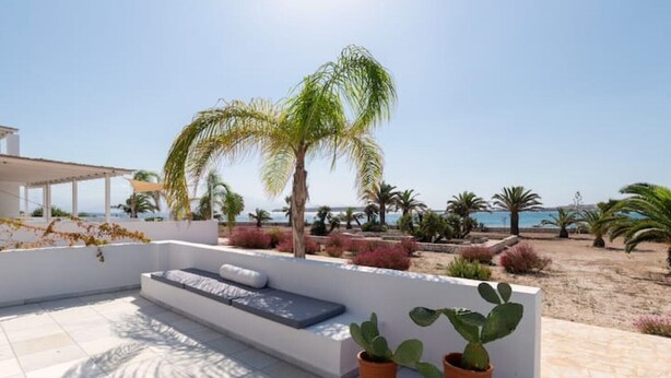 A rooftop terrace with a seating area, potted plants, and a view of the beach and sea. - The view 2 (Santa Maria Paros Νάουσα)