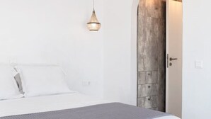 A modern bedroom with a bed, a hanging light fixture, and a wooden door. - The view 2 (Santa Maria Paros Νάουσα)