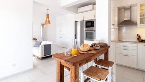 A modern kitchen with white cabinets, a wooden dining table, and a built-in oven. - The view 2 (Santa Maria Paros Νάουσα)
