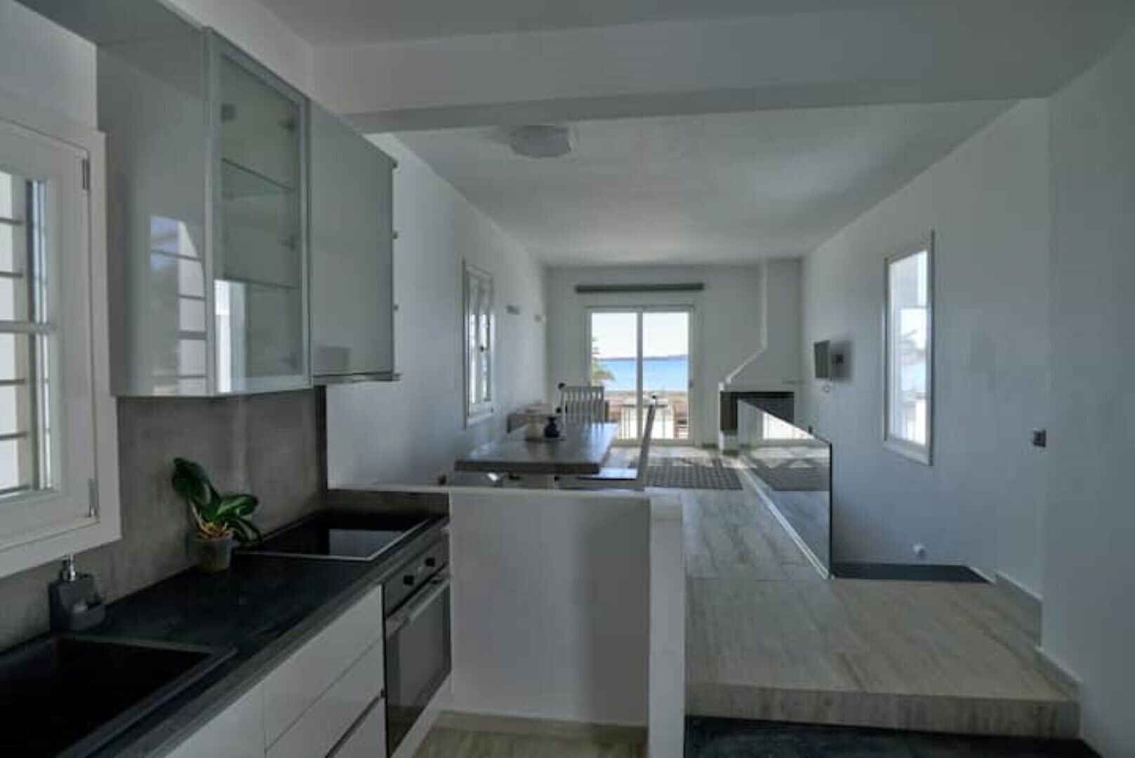 Een moderne keuken met een centraal eiland, een eethoek met uitzicht, en een trap naar een hoger niveau.