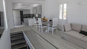 Eine moderne Küche mit weißen Schränken, ein Essbereich mit Tisch und Stühlen sowie eine Couch in einem hellen Zimmer mit einem Fenster.