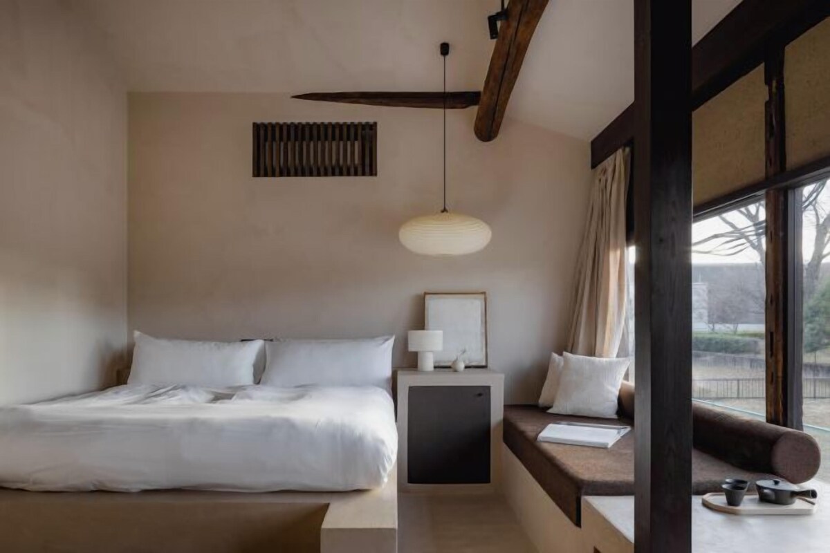 Une chambre à coucher avec un lit, une table de chevet, une lampe et une fenêtre avec des rideaux.