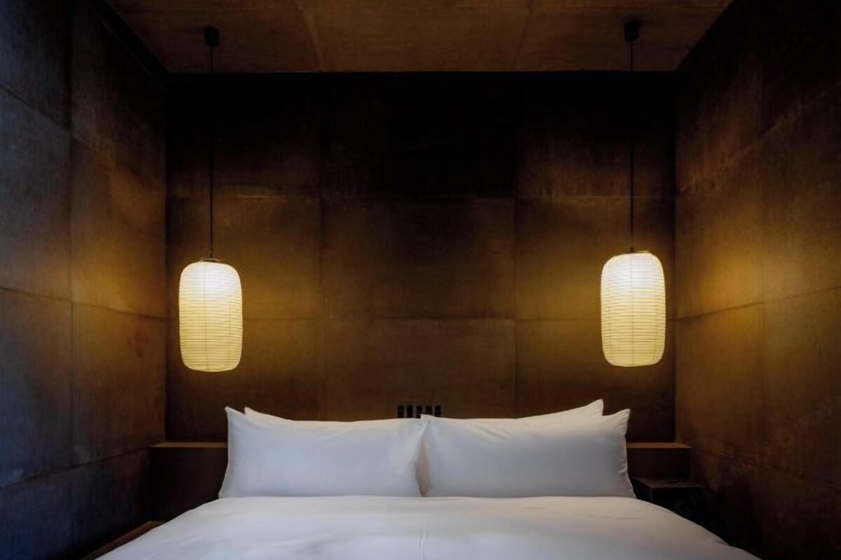 Une pièce avec un lit, deux lampes fixées au mur et un mur foncé à la texture particulière.