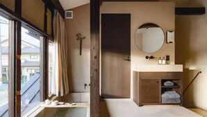 A modern bathroom with a bathtub, a sink with toiletries, and a large mirror. - Maana Kiyomizu (Kyoto)