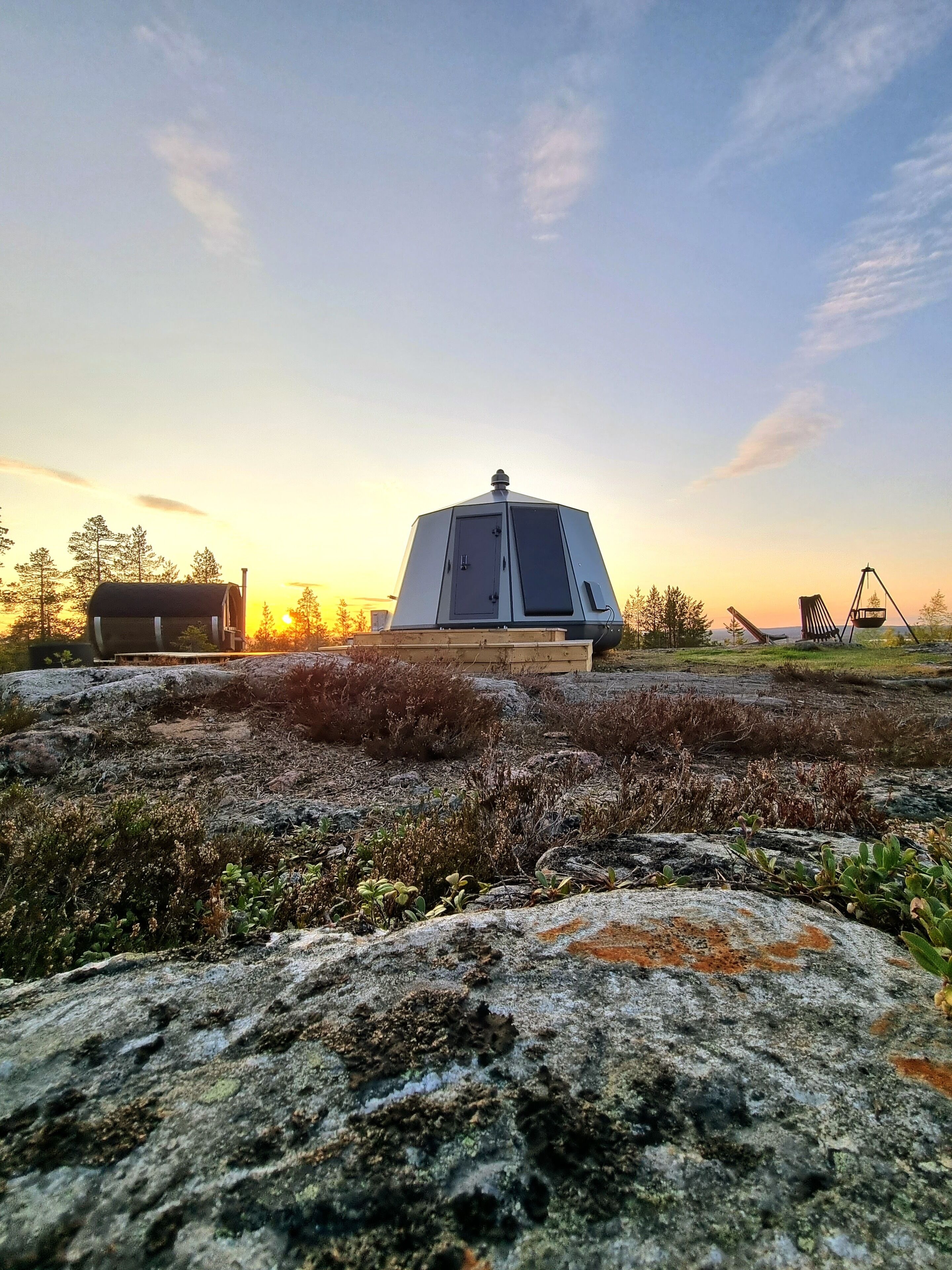 En geodisk kupolkonstruktion med en dörr och fönster, omgiven av ett stenigt landskap och gles vegetation.
