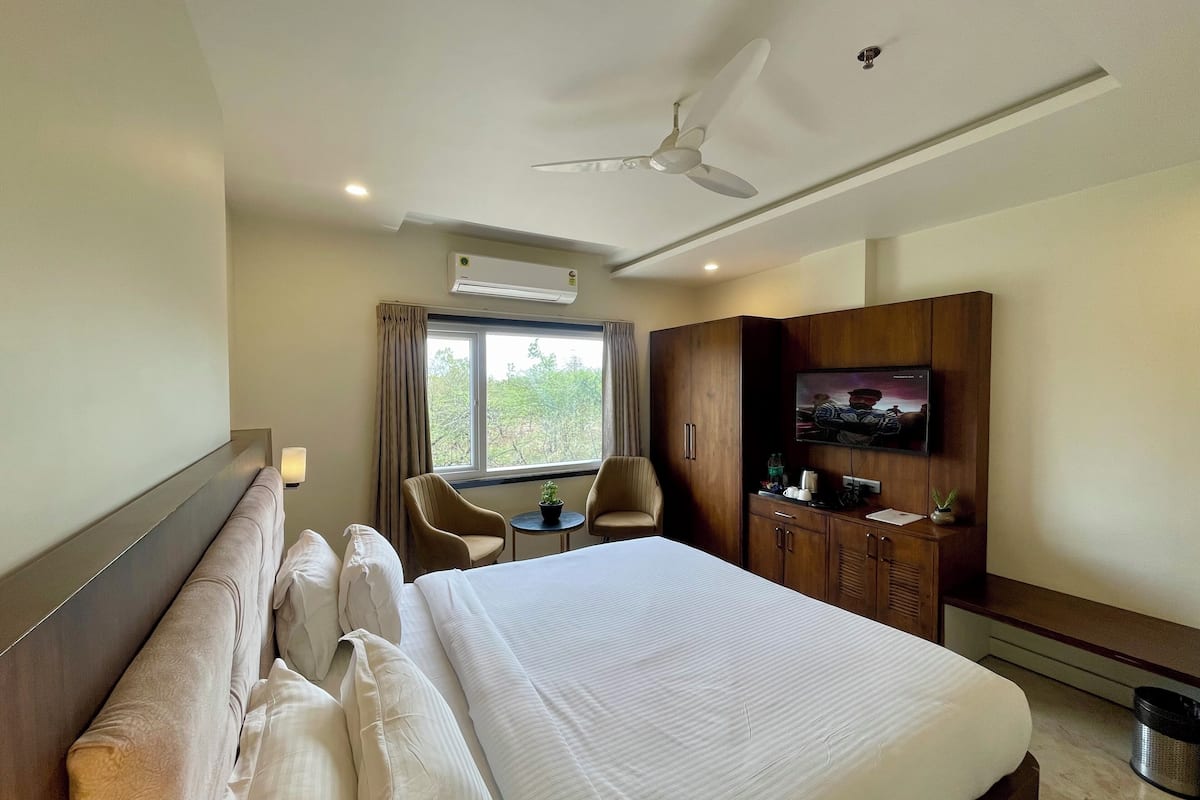 A hotel room with a large bed, a desk with a chair, a television, and a wardrobe.