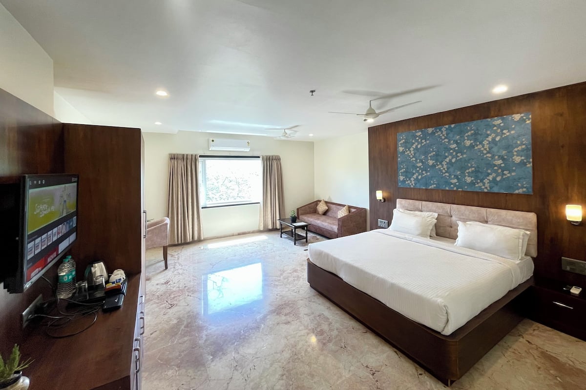 A hotel room with a bed, a TV, a desk, a chair, a sofa, and a large window.