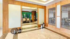 A modern lobby with a wooden wall, a glass door leading to a dining area, and a decorative metal screen. - Seasons Boutique Hotel near Sajjangarh Biological Park, Udaipur (Udaipur)