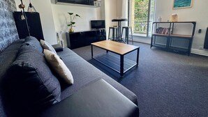 A modern living room with a sofa, coffee table, TV, and a balcony with a view. - Exceptional apartment - Seafront (Fouesnant)