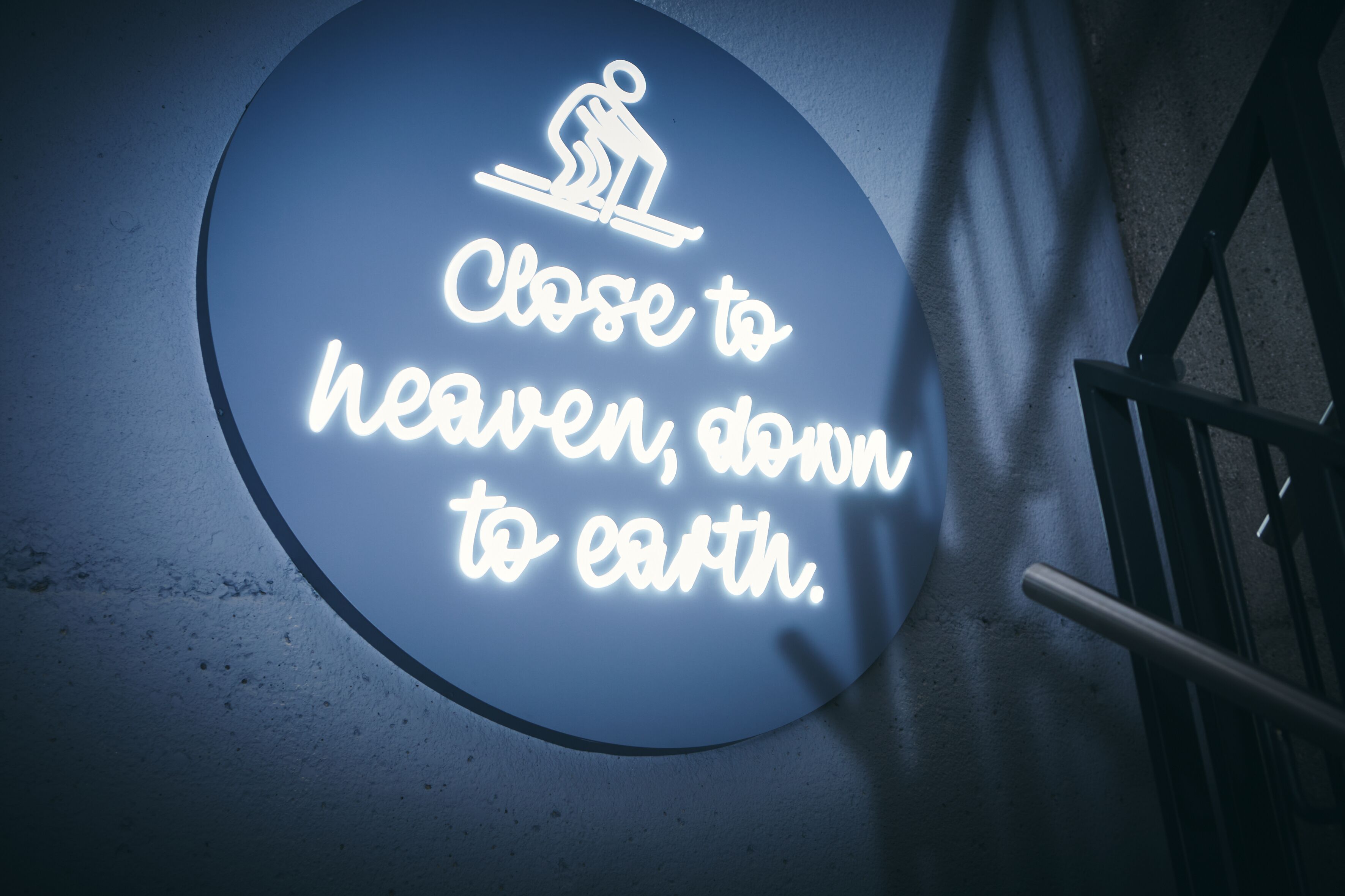 A circular neon sign with a figure skating and text that reads 'Close to heaven, down to earth.'
