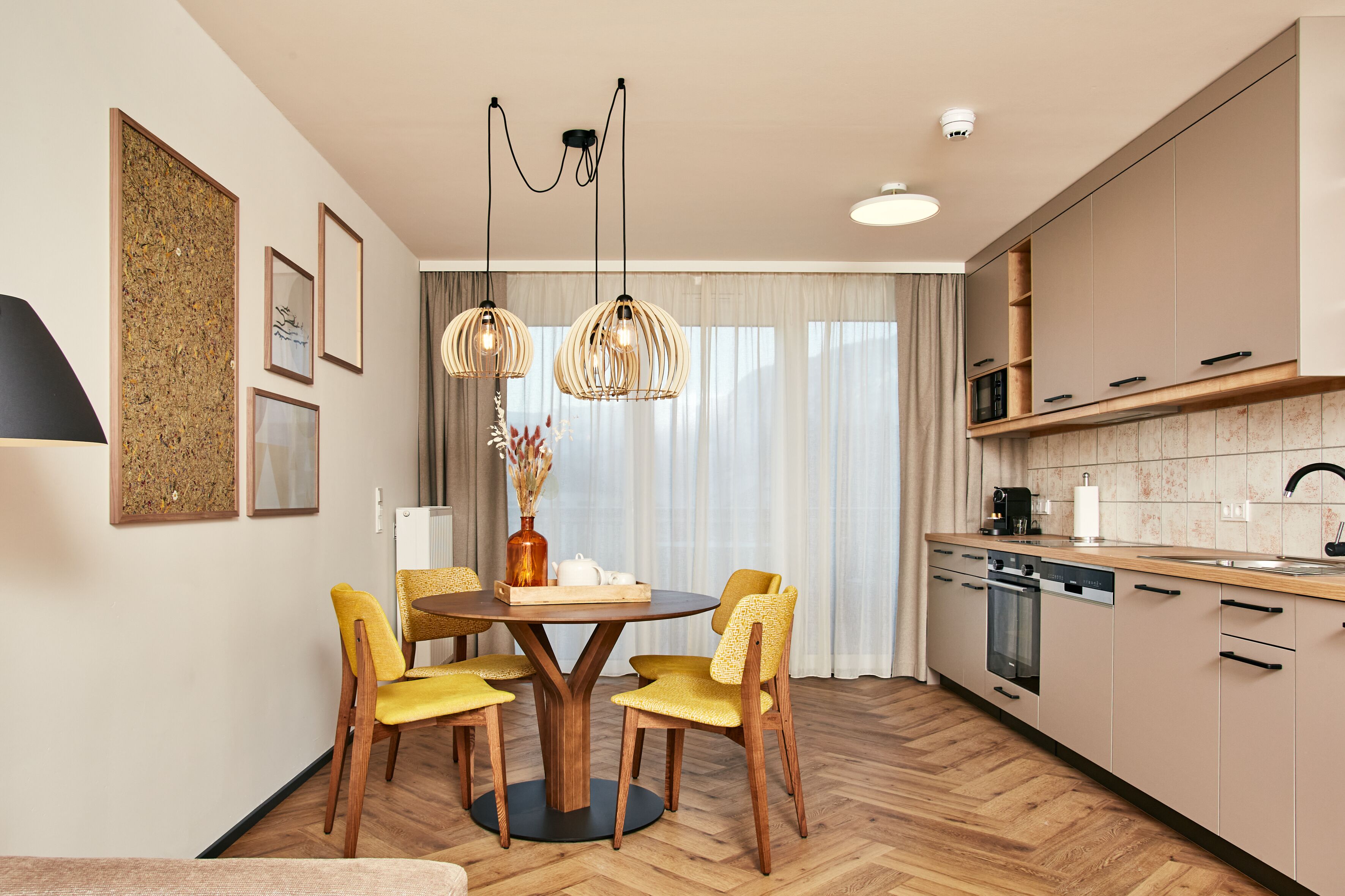 A modern kitchen with wooden cabinets, a dining area with a round table and yellow chairs, and pendant lighting.