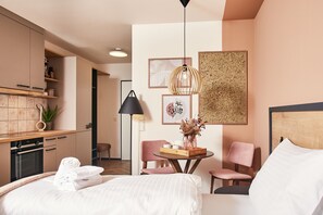 Una habitación de hotel moderna con una cama, una mesita de noche y una pequeña zona de comedor con sillas.